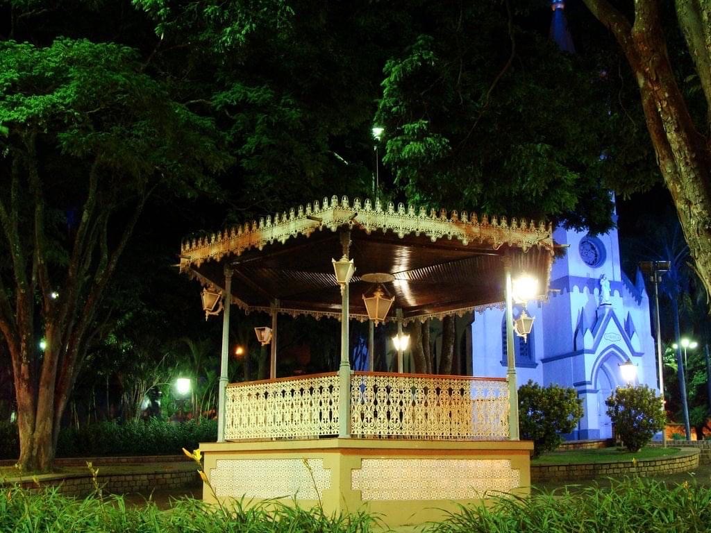 Coreto iluminado na praça central de Jaguariúna à noite, com a igreja ao fundo